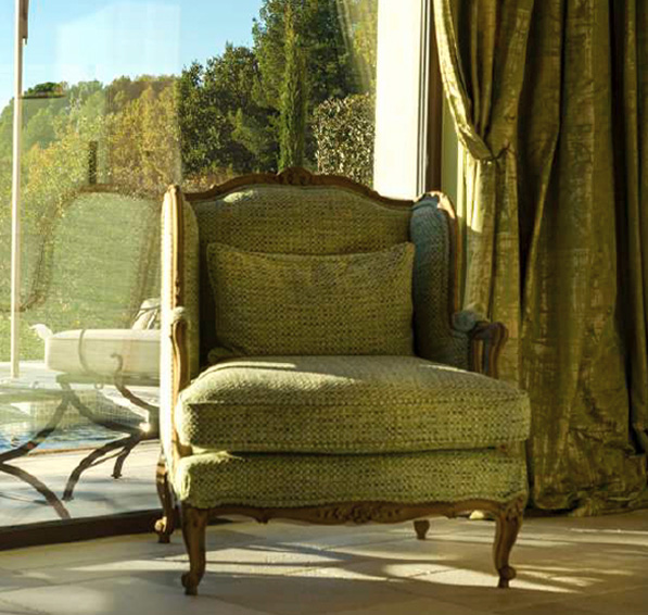 Ein eleganter, grüner Sessel steht vor großen Fenstern mit Blick auf eine malerische Landschaft.