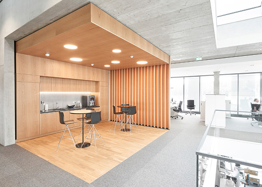 Moderne Teeküche mit Holzverkleidung und Sitzgelegenheiten in einem hellen, offenen Büro.