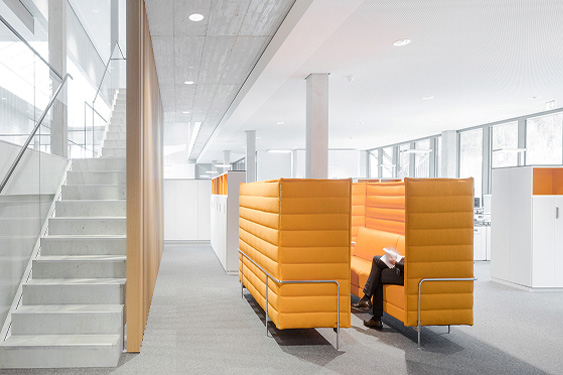 Moderne Büroumgebung mit orangefarbenen Sitznischen und einer Treppe, die zur oberen Etage führt.