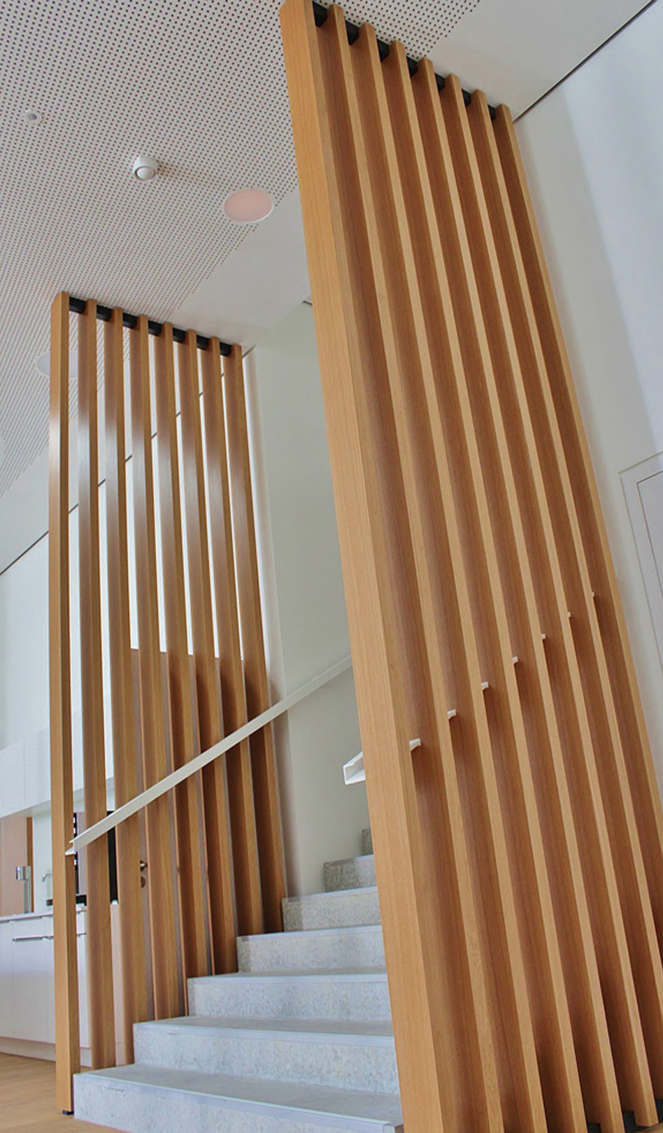 Moderne Treppe mit Holzlamellen und grauen Stufen in einem hellen, minimalistischen Raum.