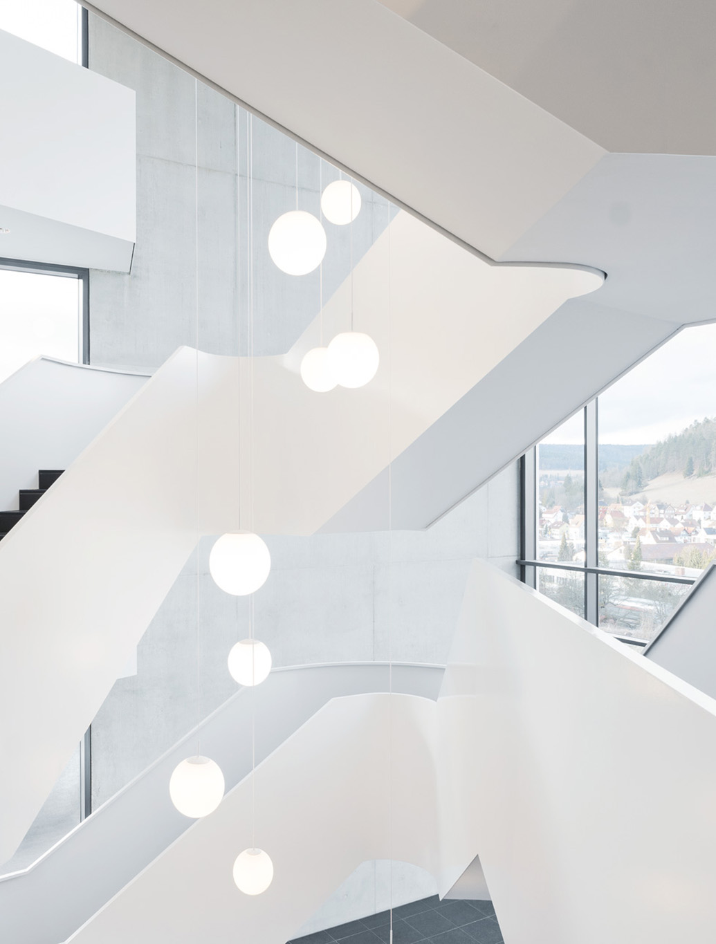 Moderne Treppe mit geschwungenen Wänden und hängenden, runden Lampen in einem hellen, minimalistischen Raum.