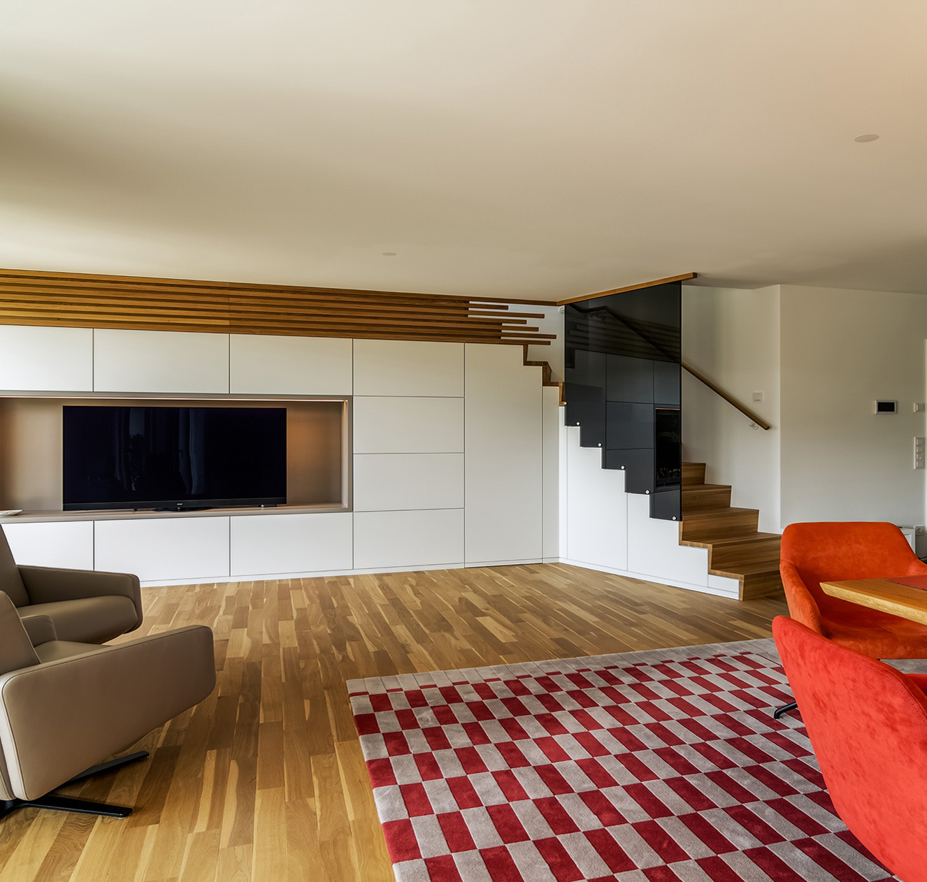 Modernes Wohnzimmer mit Holzfußboden, TV-Wand, eleganter Treppe und stilvollen Möbeln in Süddeutschland.