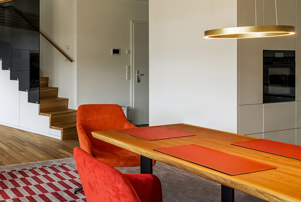 Modernes Esszimmer mit Holzstisch, roten Stühlen und eleganter Beleuchtung in einem Privathaus in Süddeutschland.