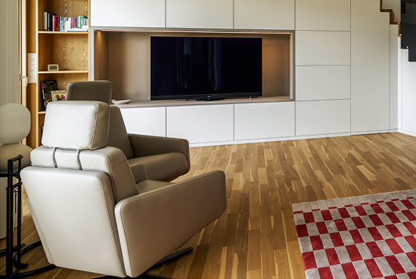Moderne Wohnlandschaft mit einem bequemen Sessel, einem Fernseher und einem stilvollen Holzboden in einem Privathaus.