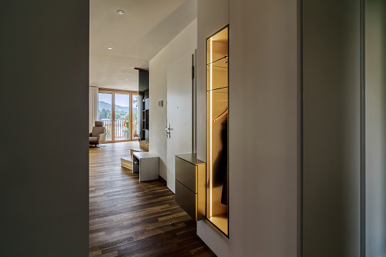 Heller Flur mit Holzfußboden, moderner Garderobe und Zugang zu einem Balkon mit Blick auf die umliegende Landschaft.