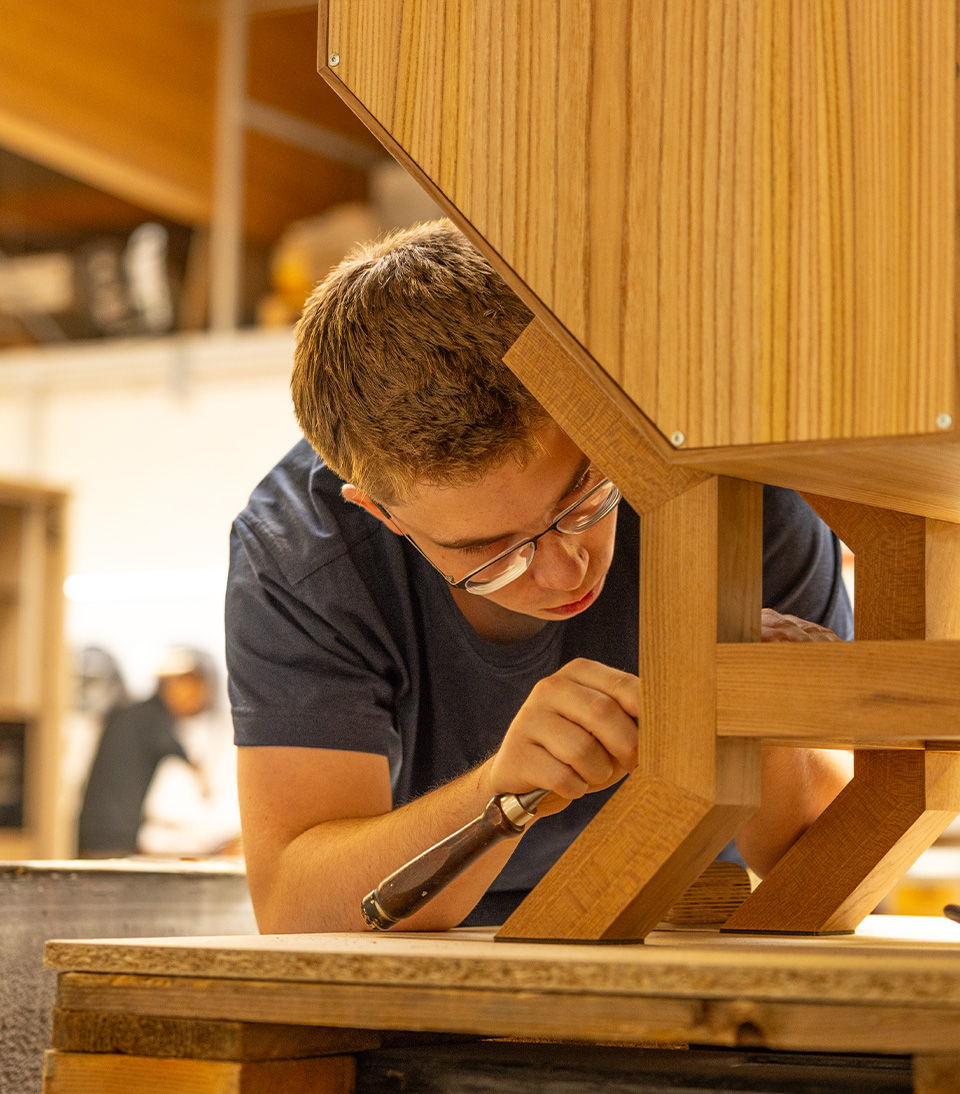 Ein junger Handwerker bearbeitet sorgfältig ein Holzstück in einer Werkstatt.